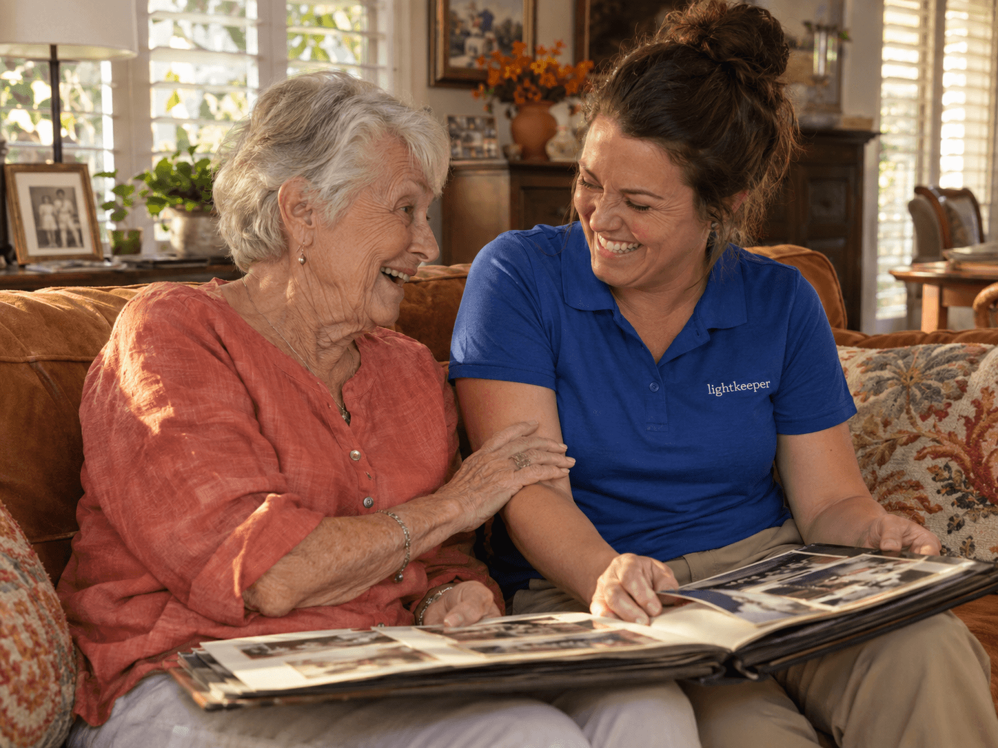 An older woman sharing a laugh and a family photo album with a caregiver in a cobalt Lightkeeper polo