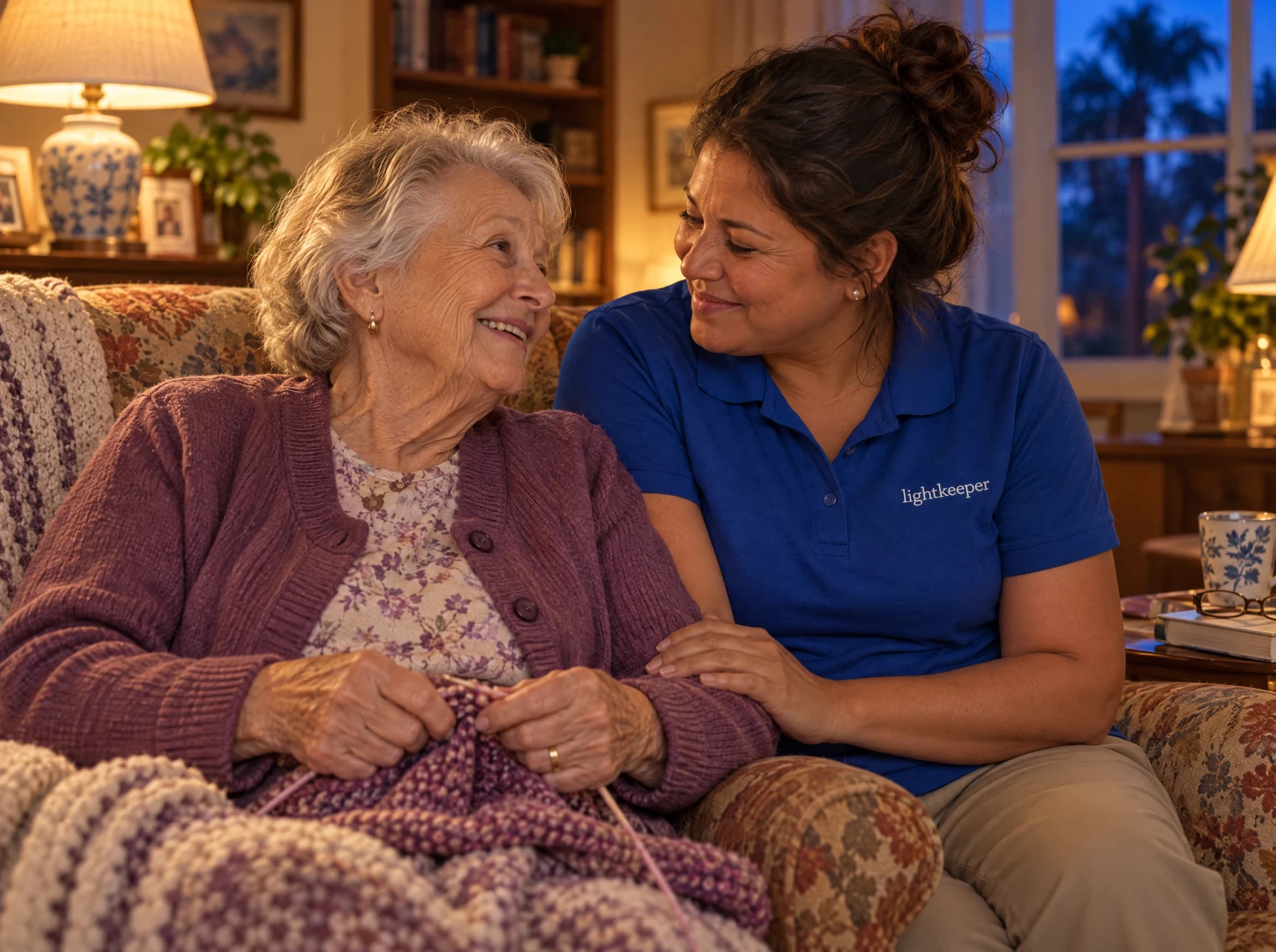 An older woman and her Lightkeeper share a quiet conversation in a warmly lit room at dusk